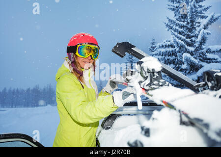 Ritratto di giovane donna sci di fissaggio sul tetto della vettura dopo il viaggio di sci durante la nevicata Foto Stock