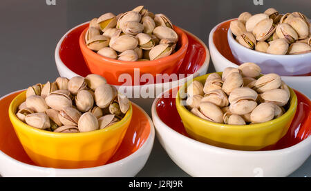 Calorie deliziosi pistacchi noci avvolte in una ciotola colorata inseriti uno nell'altro su sfondo grigio di tavolo in vetro Foto Stock