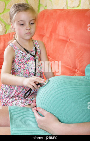 Figlia medico utilizzando uno stetoscopio esaminando bianco donna incinta. Foto Stock