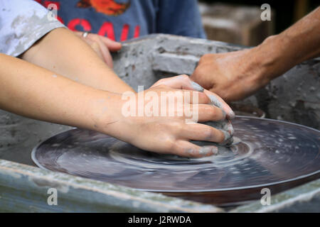 Atelier di ceramica, di insegnamento in ceramica. Un grumo di creta bagnata comincia a prendere forma come un giovane bambino stampi su un tornio del vasaio, con spettatore in background. Foto Stock