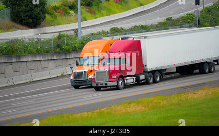 Due camion rosso e arancione, vecchi e nuovi e classici e moderni camion di diverse generazioni e modelli stanno lavorando insieme su autostrada trasporto di merci Foto Stock