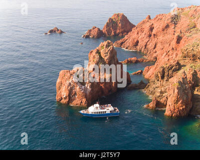 VISTA AEREA. I turisti su una barca turistica ammirando la spettacolare roccia rossa di Cap du Dramont. Saint-Raphël, Var, Costa Azzurra, Francia. Foto Stock
