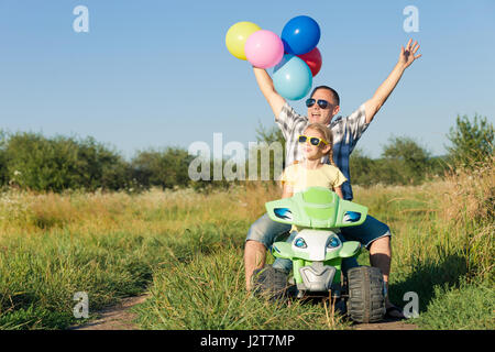 Padre e figlia giocando con palloncini sulla strada al giorno. Essi guida su quad bike nel parco. Le persone aventi il divertimento sulla natura. Concetto Foto Stock