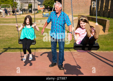 Ritratto orizzontale di ragazze essendo spinto sul oscilla con il loro nonno in un parco. Foto Stock