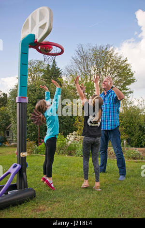 Vista verticale di un nonno giocare a basket con i suoi nipoti in giardino. Foto Stock