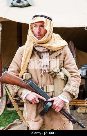 Inghilterra, sandwich. Saluto alla 40s evento. Rievocazione ratti nel deserto vita Storia Gruppo, soldato in piedi con la testa di arabo-abito, Esercito Britannico uniforme del deserto e la pistola di tommy in entrambe le mani. Affacciato ma nessun contatto visivo. Foto Stock