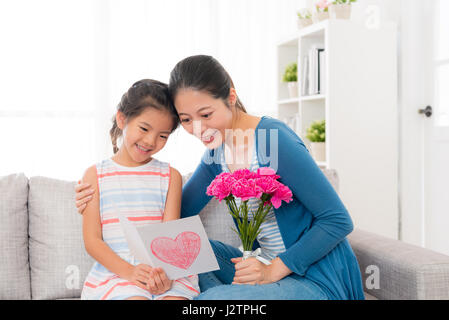 Asian donna cinese tenendo un mazzo di fiori di colore rosa con incantevole piccola ragazza seduta insieme sul divano insieme guardando la scheda Contenuto e gif Foto Stock