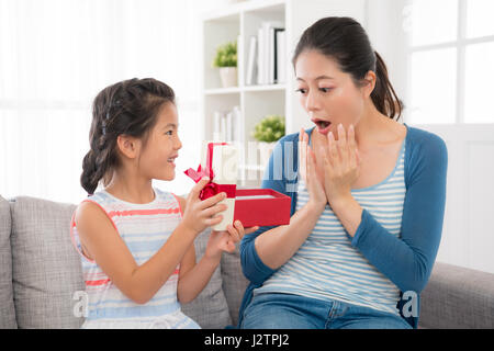 Asian graziosa bambina invio dono nastro rosso confezione regalo per il preferito mom nella giornata della madre sua mamma è stato sorpreso e incredibile seduta su th Foto Stock