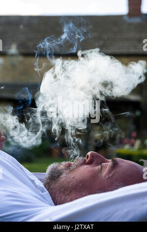 Un uomo di mezza età gode di un sigaro in giardino Foto Stock