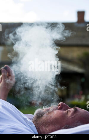 Un uomo di mezza età gode di un sigaro in giardino Foto Stock