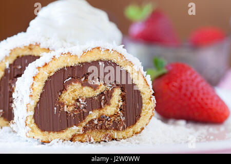 Fetta di cioccolato torta di noci di cocco roll decorate con ehipped panna e fragole, primo piano. Foto Stock