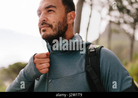 Ritratto di sano giovane uomo in piedi all'aperto e guardando lontano. Bel giovane maschio in runner sportswear. Foto Stock