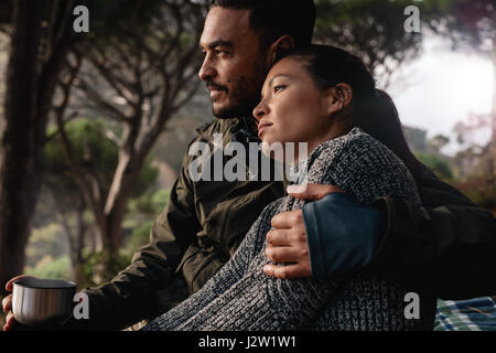 Giovane uomo e donna seduta all'aperto e guardando lontano. Coppia giovane appoggiata all'aperto con una tazza di caffè. Foto Stock