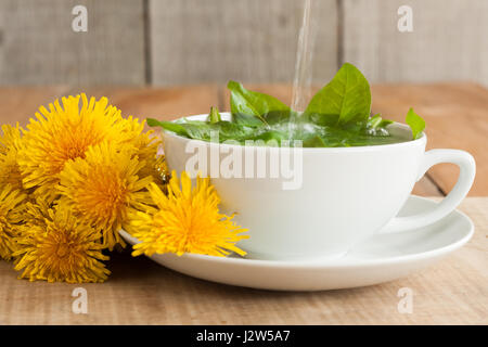 La preparazione di tarassaco tè versando acqua calda al di sopra di foglie fresche di dente di leone Foto Stock
