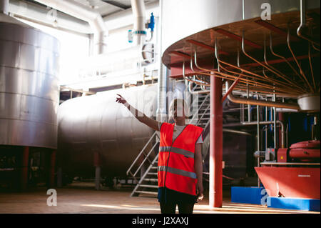 Lavoratore di sesso femminile che sulla fabbrica di birra. ritratto donna in accappatoio, permanente sulla linea di sfondo della produzione alimentare, il controllo di gestione di apparecchiature di controllo per il processo di produ Foto Stock