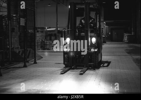 Dipendente del magazzino in tute vestiti, driver Reachtruck occupato a lavorare sulla logistica spostando sul caricatore su pallet con barili di birra sulla linea di fabbrica per pro Foto Stock