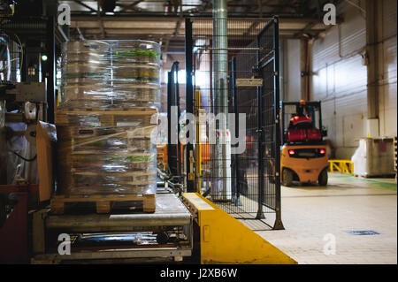 Dipendente del magazzino in tute vestiti, driver Reachtruck occupato a lavorare sulla logistica spostando sul caricatore su pallet con barili di birra sulla linea di fabbrica per pro Foto Stock