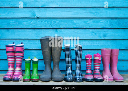 Molti stivali in gomma colorati davanti a una parete di legno blu Foto Stock