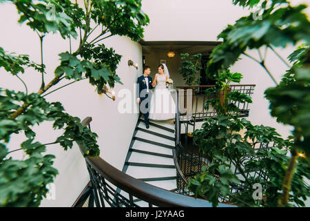 Felice sposa e lo sposo andando giù per le scale. Pianta verde foglie su un primo piano Foto Stock