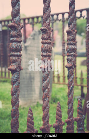 Un vecchio oggetto contrassegnato per la rimozione definitiva si siede dietro un arrugginito recinzione in ferro in un cimitero. Foto Stock