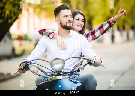 Coppia giovane riding scooter insieme mentre donna felice rivolto lontano e sorridente Foto Stock