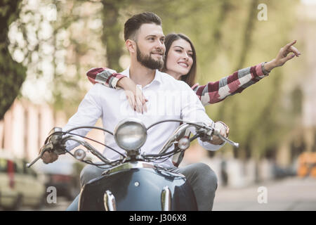 Coppia giovane riding scooter insieme mentre donna felice rivolto lontano e sorridente Foto Stock