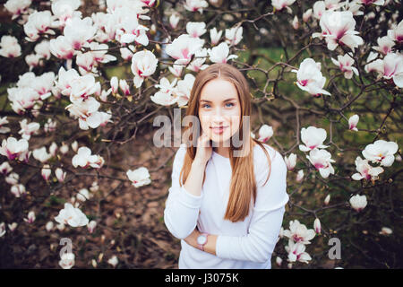 Bella donna in posa e magnolia bianco nel parco. Sfondo di primavera Foto Stock