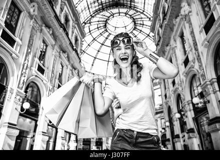 Scopri le più inaspettate tendenze a Milano. Ritratto di sorridere moda donna con occhiali colorati e borse per lo shopping in Galleria Vittorio Emanuele I Foto Stock