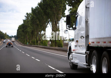 Moderno semi-camion bianco che si riflette su una superficie a specchio tutto intorno con un rimorchio che si muove su un'ampia autostrada che si estende fino alla distanza Foto Stock