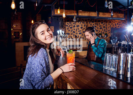 Una ragazza con cocktail di sorrisi dietro il contatore al bar Foto Stock