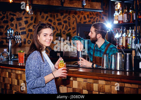 Una ragazza con cocktail di sorrisi dietro il contatore al bar Foto Stock