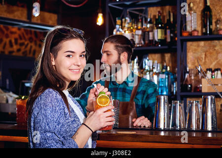 Una ragazza con cocktail di sorrisi dietro il contatore al bar Foto Stock