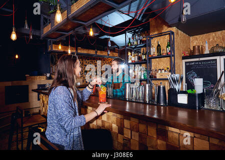 Una ragazza con cocktail di sorrisi dietro il contatore al bar Foto Stock