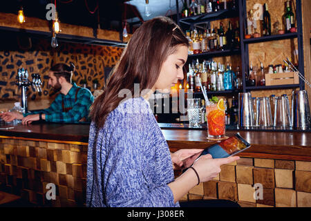 Una ragazza con cocktail di sorrisi con la compressa dietro il contatore al b Foto Stock