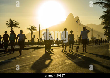 RIO DE JANEIRO - Febbraio 12, 2017: sagome di brasiliani di passeggiare lungo la spiaggia Avenida Vieira Souto street a Ipanema al tramonto. Foto Stock