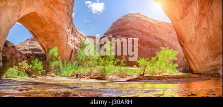Ampio angolo di visione di due escursionisti backpacking sotto splendide Jacob Hamblin Arch in Coyote Gulch in una giornata di sole con cielo blu e nuvole in estate, Grand Foto Stock