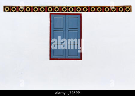 Chiuso persiane blu della finestra con maroon windowframe sulla parete dipinta di bianco della kuti-edificio per la vita dei monaci in Wat Xang Khong Foto Stock