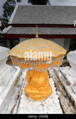 Statua dorata di Budha seduti sotto golden ombrello in Wat Pa foresta Phai-Bamboo monastero riccamente decorate con pitture murali in stile Thai-Lao raffiguranti Foto Stock