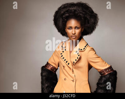 Licenza e stampe a MaximImages.com - Ritratto di bellezza edgy di alta moda di una donna nera afroamericana che indossa un cappotto arancione con pelliccia nera su g Foto Stock