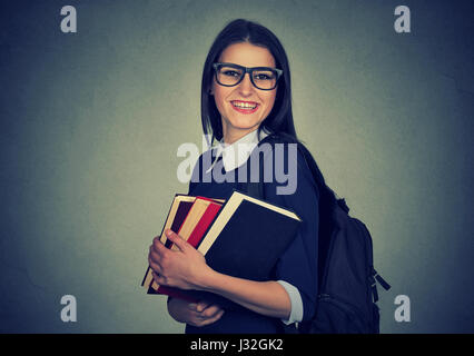 Studente sorridente che porta uno zaino e azienda pila di libri Foto Stock