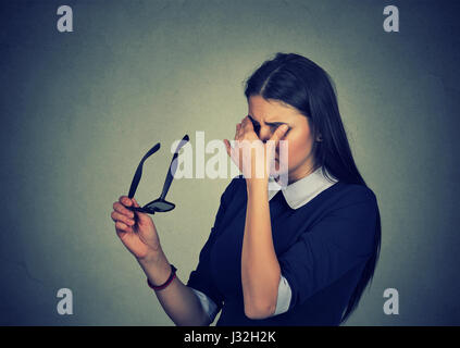 Donna con gli occhiali strofinando i suoi occhi si sente stanco isolato sul muro grigio Sfondo. Ragazza giovane che soffre di una malattia degli occhi problema Foto Stock