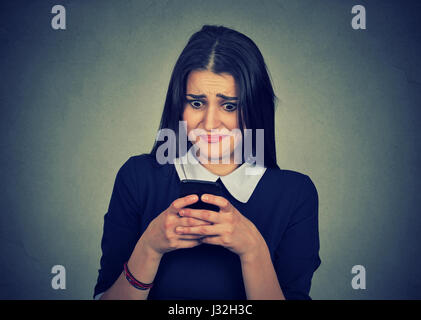 Ritratto ansiosi infastiditi donna guardando il suo telefono cellulare vedendo cattivo messaggio isolato su sfondo grigio. Le emozioni umane faccia espressione Foto Stock