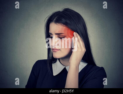 Il tinnito. Primo piano alto profilo laterale malati femmina presentando un dolore alle orecchie di toccare la sua testa doloroso tempio colorato in rosso isolato sul muro grigio sfondo Foto Stock