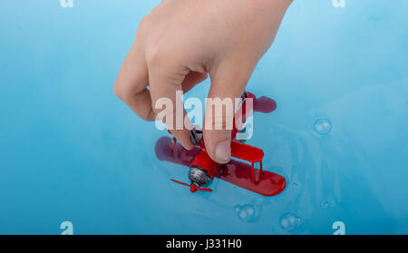 Mano che regge un modello di aereo e un uomo statuetta in acqua blu Foto Stock