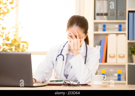 Incredibile scioccato giovane donna medico sento mal di testa in seduta clinica ufficio. razza mista asiatica modello cinese. medico e sanitario concetto. Foto Stock