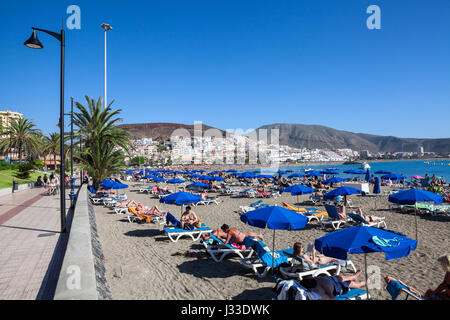 Di Los Cristianos, Tenerife, Canarie, Spagna -€" circa gen, 2016: persone prendere il sole sulla famosa spiagge urbane con sabbia fine. Blue ombrelloni e lettini sono a Foto Stock