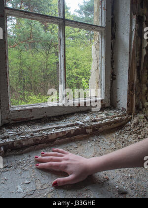 Una mano con dipinti di rosso le unghie con distrutta finestra in legno in uno sfondo Foto Stock