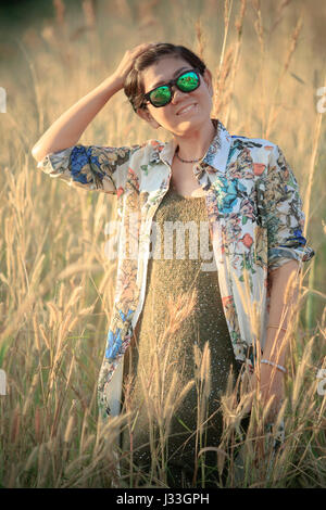 Ritratto di 40s donna asiatica che indossa bellissimi vestiti alla moda in piedi in campo in erba e rilassante toothy sorridente Foto Stock