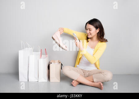 Giovani asiatici sorpreso donna seduta oltre alla fila di borse per lo shopping, felice con le nuove scarpe Foto Stock