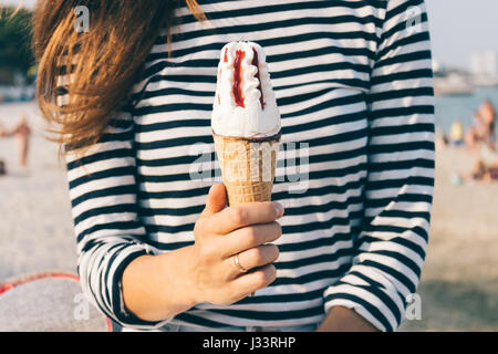 Close-up di una donna che mantiene il gelato in mano. La donna in un striped T-shirt è in appoggio su una spiaggia d'estate. Foto Stock